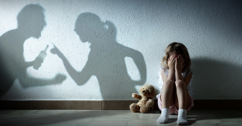 child cowering with shadow of parents arguing on wall