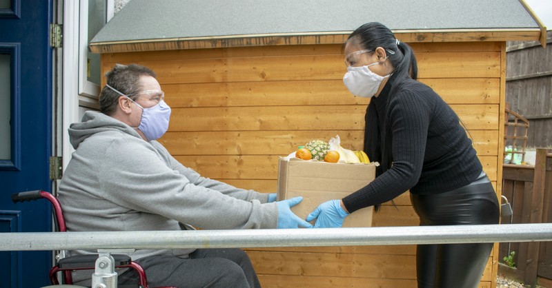 woman helping during coronavirus in face mask delivering groceries to man in wheelchair in face mask