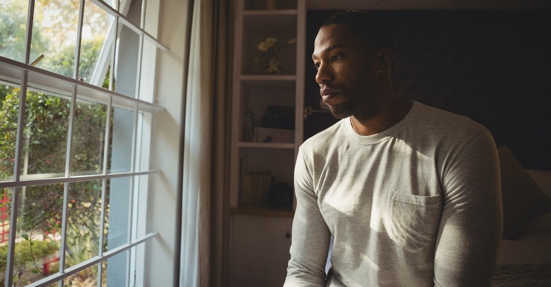 sad man standing near window thinking lonely thoughts