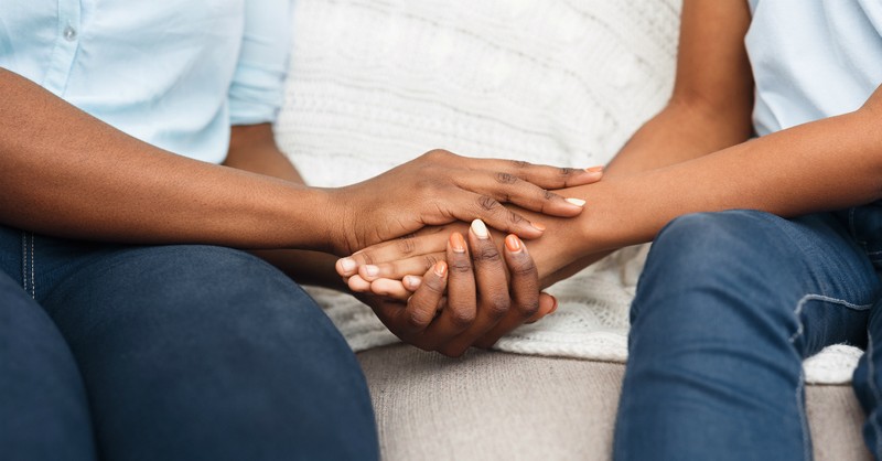 mom hands holding tween kid hands on couch comforting