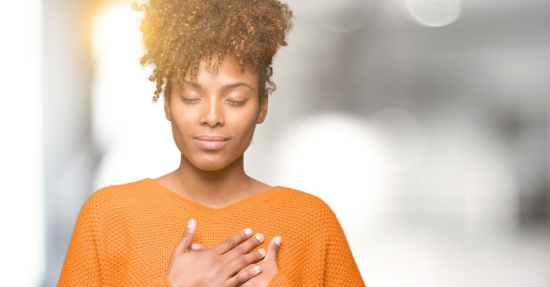 Peaceful woman with eyes closed and hands over her heart