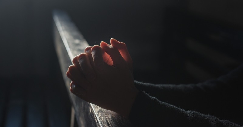 Praying hands in a dark pew