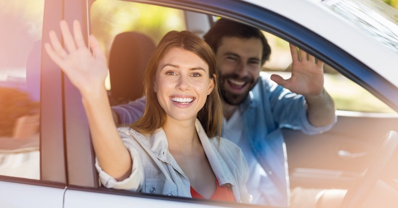 couple waving out of car window smiling happy