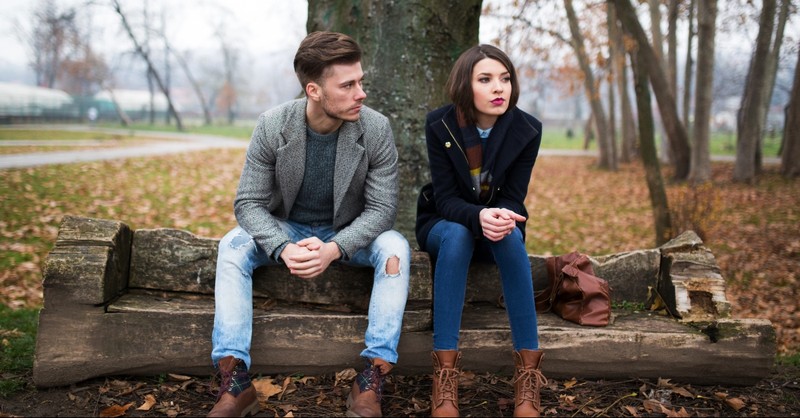 Man and woman sitting in a park looking mad