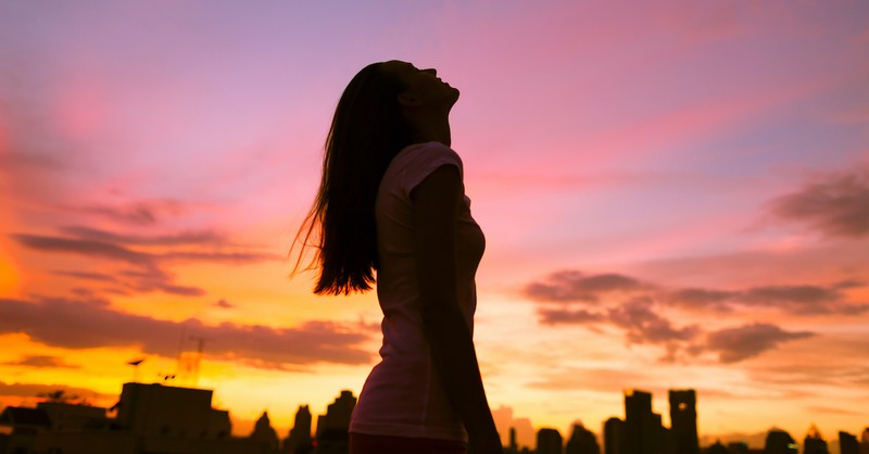 silhouette of woman looking up at sky during sunset against cityscape, goodness of god