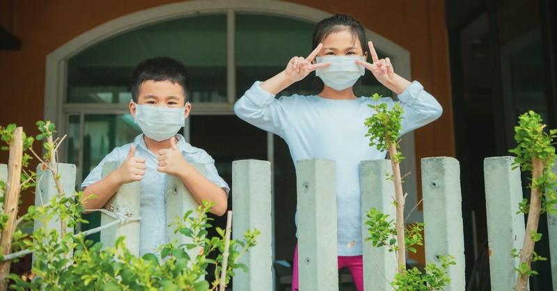 two children waving from house wearing masks