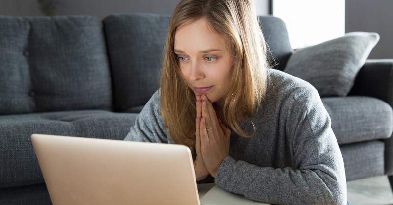 woman praying while watching video on laptop computer