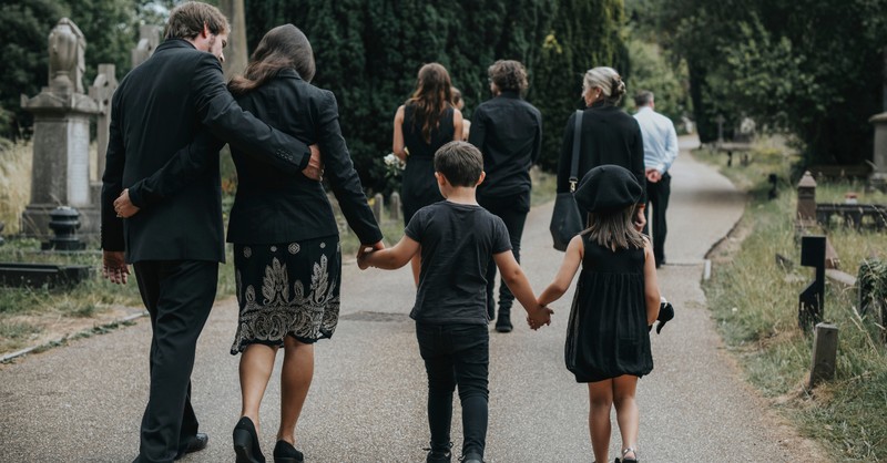 family walking away after funeral in cemetery grieving