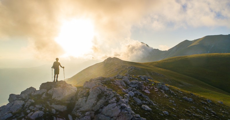 back view of man climbing over mountain range at sunrise, wonderful time to be alive