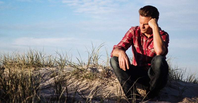 man sitting on beach thinking wondering pensive