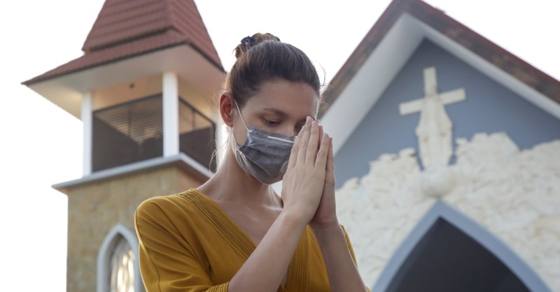 woman with coronavirus mask on praying outside church