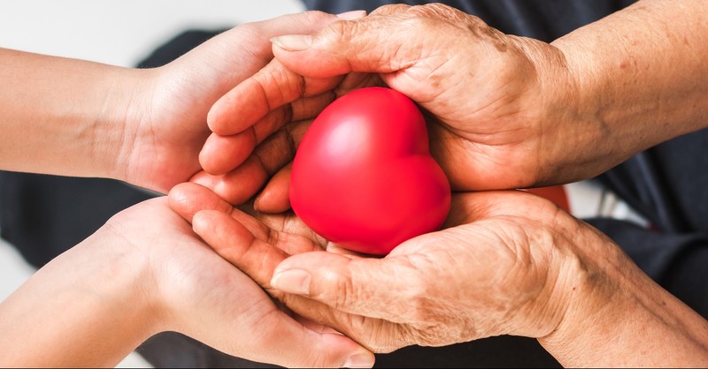 Young hands around old hands holding a toy heart