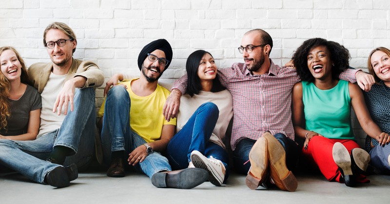 multicultural diverse row of friends sitting against wall arms over shoulders smiling