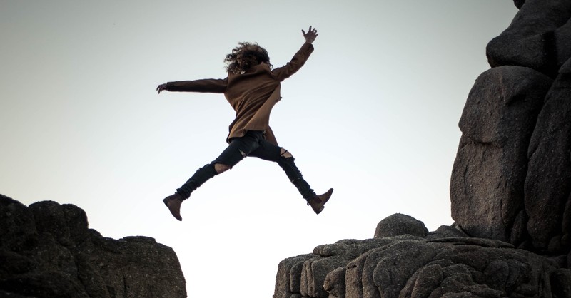 woman jumping over a rocky chasm