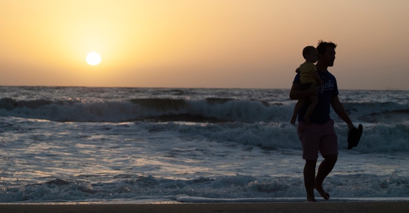 dad holding baby at sunset walking along beach shore