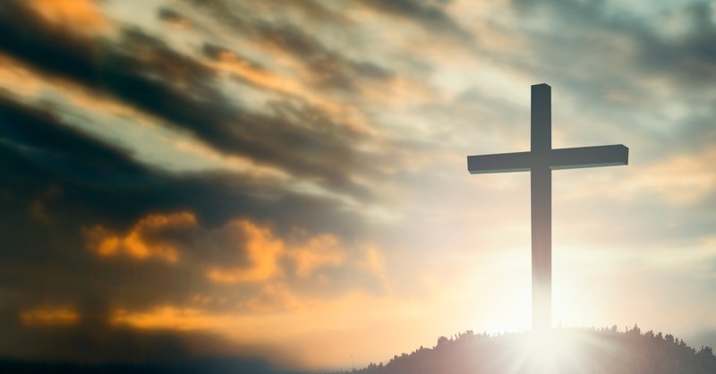 Jesus cross on hilltop sunrays at dusk