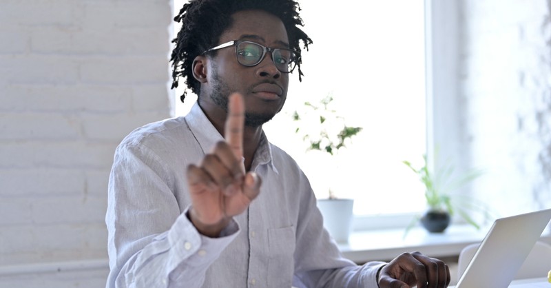 man pointing finger at camera working at laptop