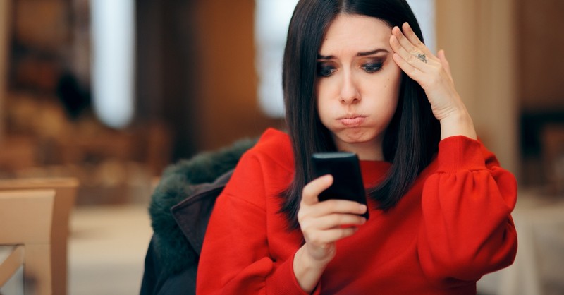 woman looking worried at phone sitting in a restaurant, red flags to not ignore while dating