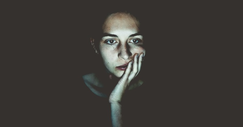 woman looking unsure or distressed in a dark space with electronic light on her face, moving beyond shame