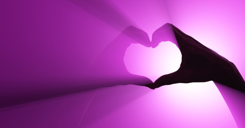 hands making heart shape with purple light shining through