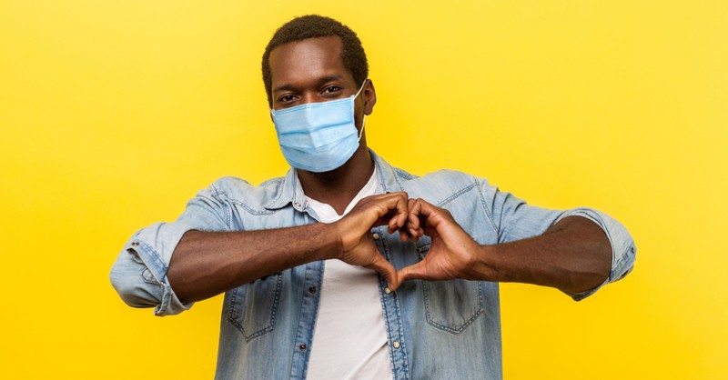man wearing face mask making love heart sign over his heart