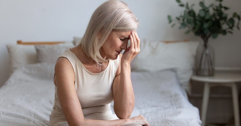 senior white woman looking ill or in pain sitting on bed, how to find relief when hurting