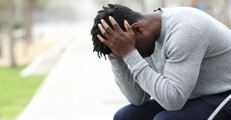 sad man overwhelmed head in hands on bench