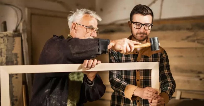 senior man teaching younger man carpentry mentor in retirement