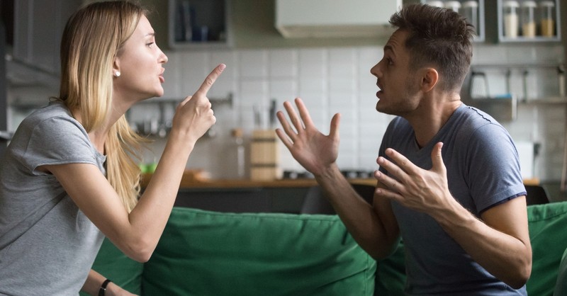 husband and wife arguing with each other on couch looking angry