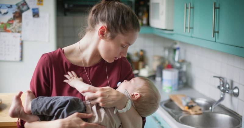 Mother embracing sleeping baby son in kitchen