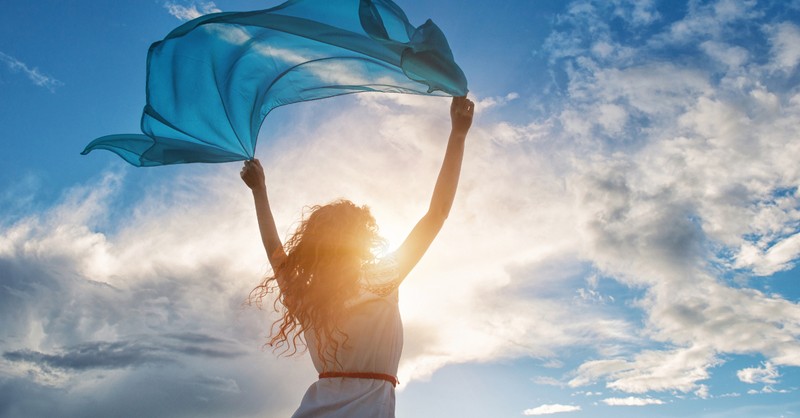 woman raising blue scarf against blue sky praising God in nature