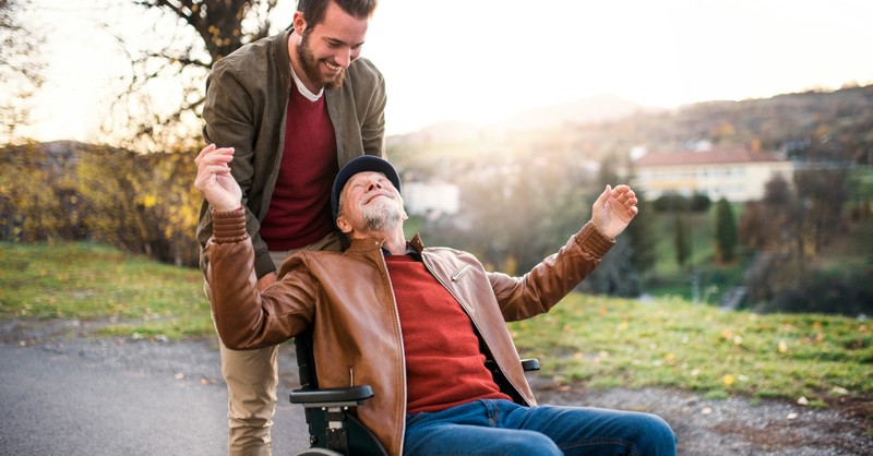 man pushing senior in wheelchair outdoors smiling