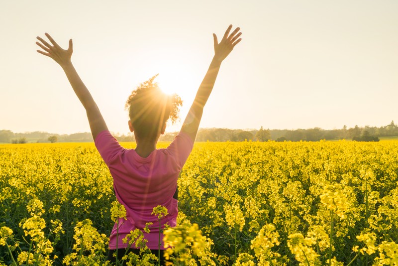 woman arms up in yellow wildflower field in praise gratitude and celebration