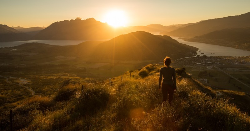 woman standing on hillside overlooking valley as sun rises