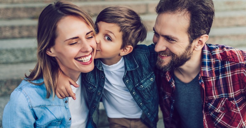 mom and dad hugging young son kissing mom