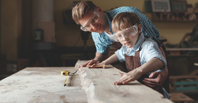 dad and son with safety glasses on working on carpentry in garage