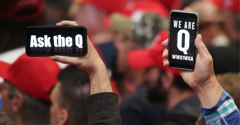 QAnon signs on phones, QAnon started with a post on a messaging board