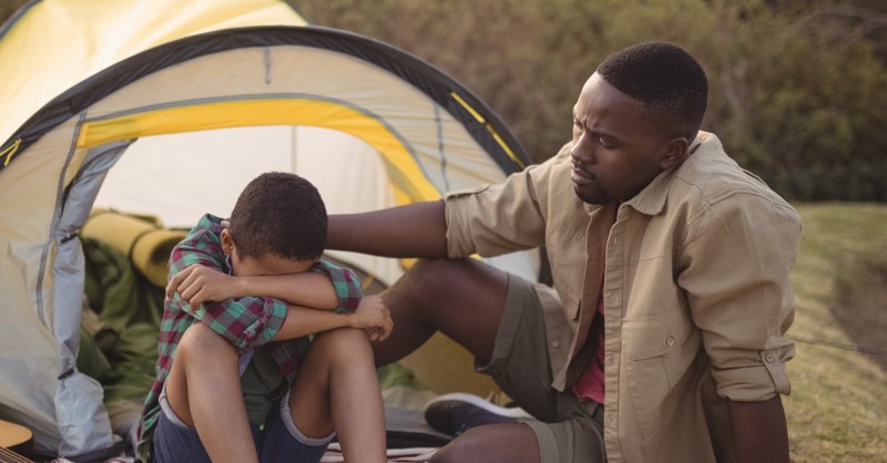 dad consoling crying tween son camping together