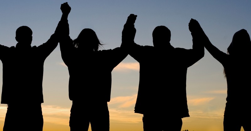 back view of family with hands joined and raised at sunrise