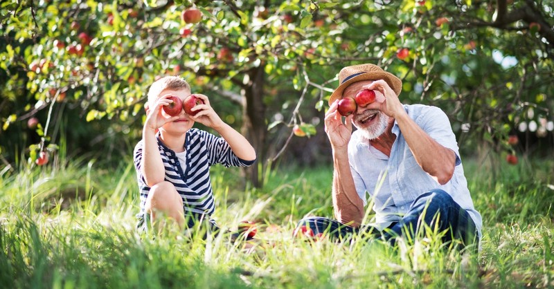 grandfather and grandson holding apples up to their eyes sitting in an orchard, reasons God refers to you as the apple of his eye