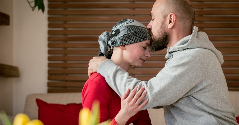 husband kissing wife in cancer treatment on forehead