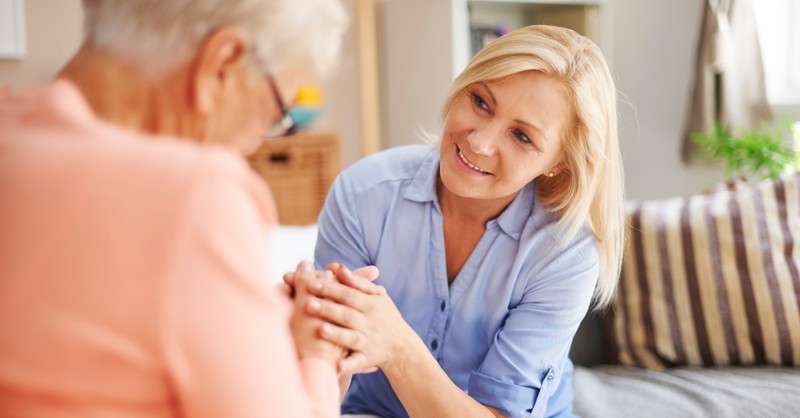 mature woman holding hand of senior mom in reassurance listening