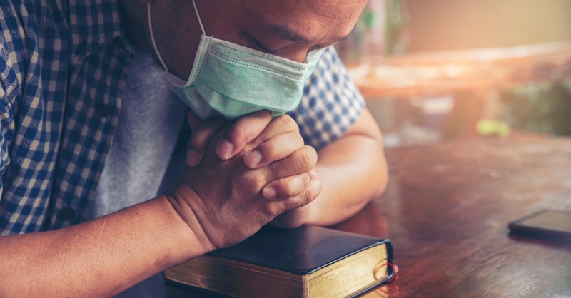 man in face mask praying on bible for pastor appreciation month