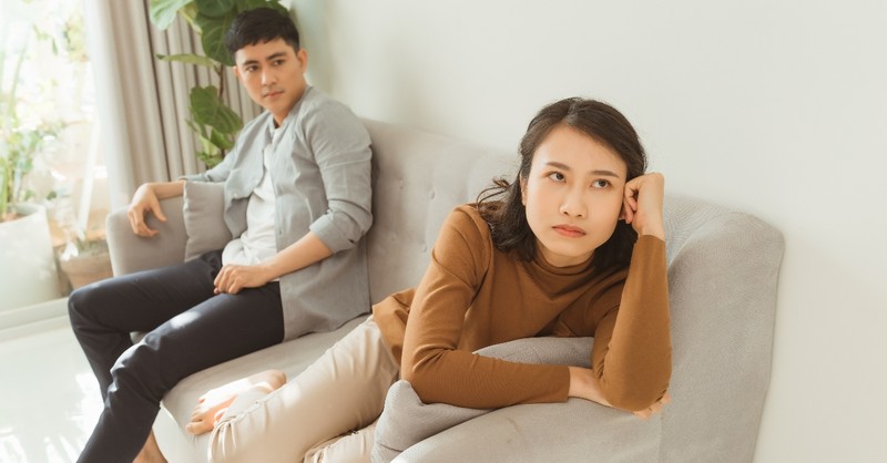 wife looking upset with husband looking away on couch, ways you're making conflict in marriage harder for yourself