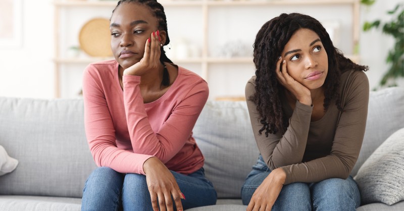 Two women sitting next to each other on a couch, looking unhappy