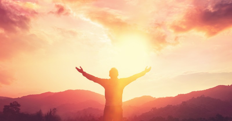 man arms wide in thanksgiving praise at sunset