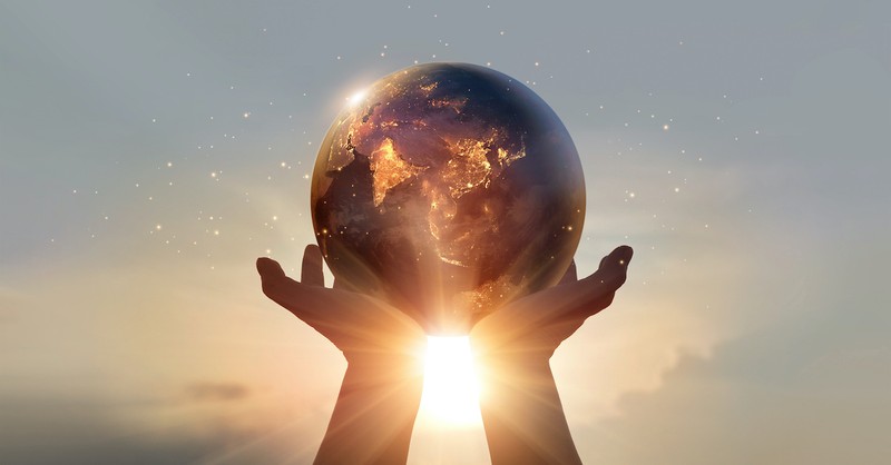 graphic of hands holding the world against sunset background