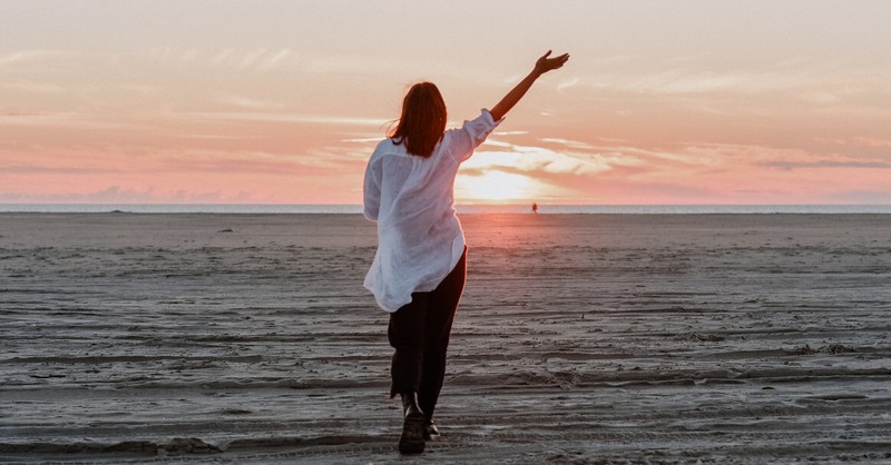 Mujer caminando en la playa vacía dando alabanzas y gracias en temporada de pérdida