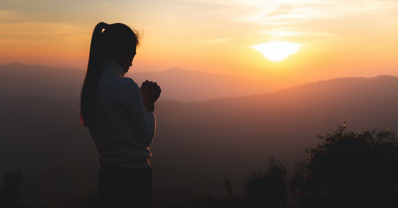 woman praying outside at sunset