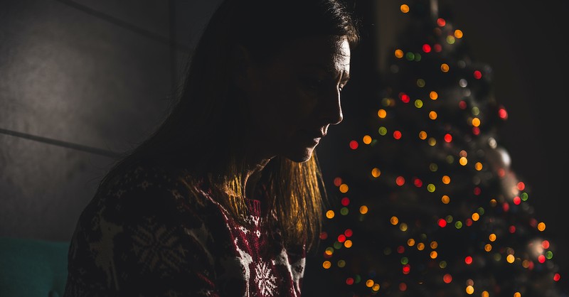 sad woman mourning at Christmas in the dark by lit Christmas tree